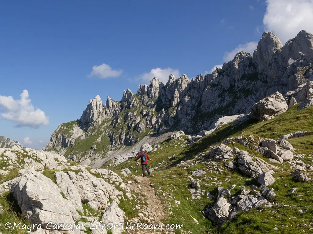 A man on a trail going through a mountain valley with big rocks and tall limestone formations