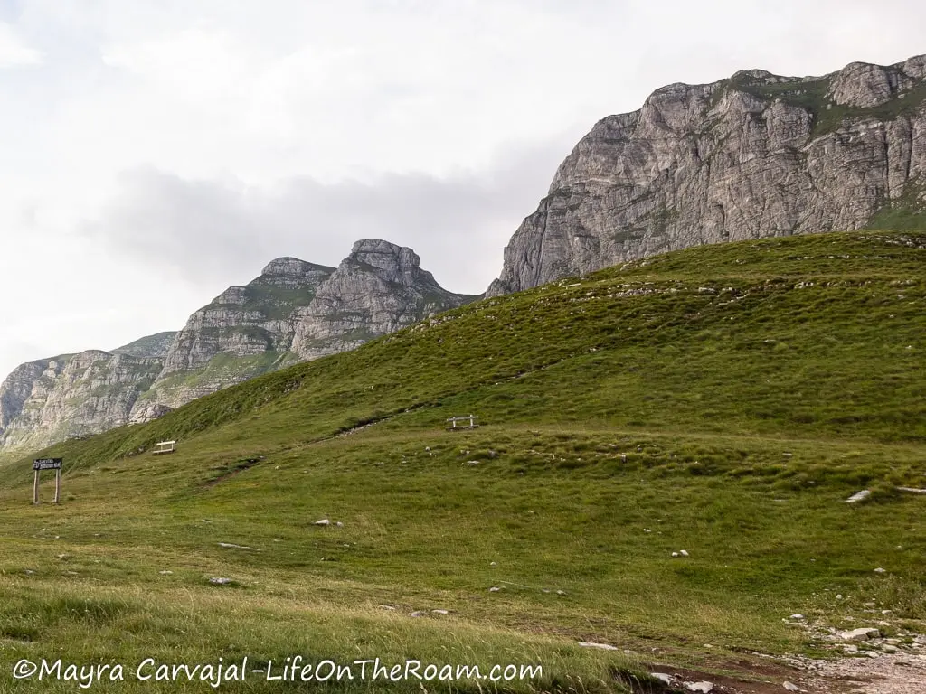 A trail along a grassy slope with limestone formations at the top