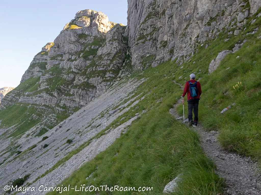 A man hiking on a trail along the edge of a mountain with scree on the slope