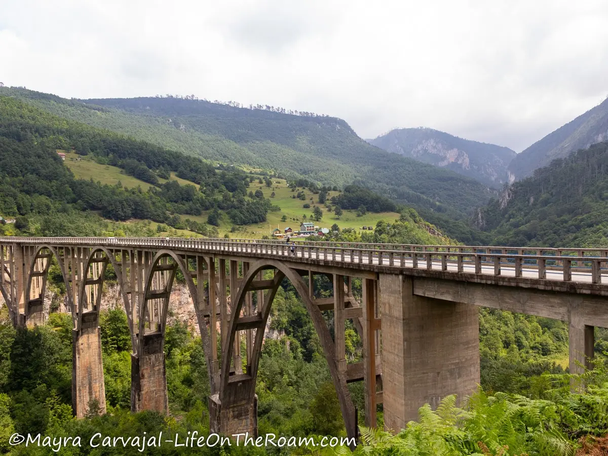 A concrete bridge supported by tall arches with mountains in the background