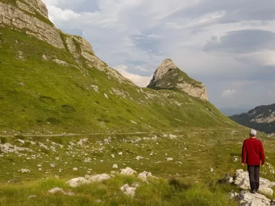 A man walking on a trail alongside a mountain covered in grasses