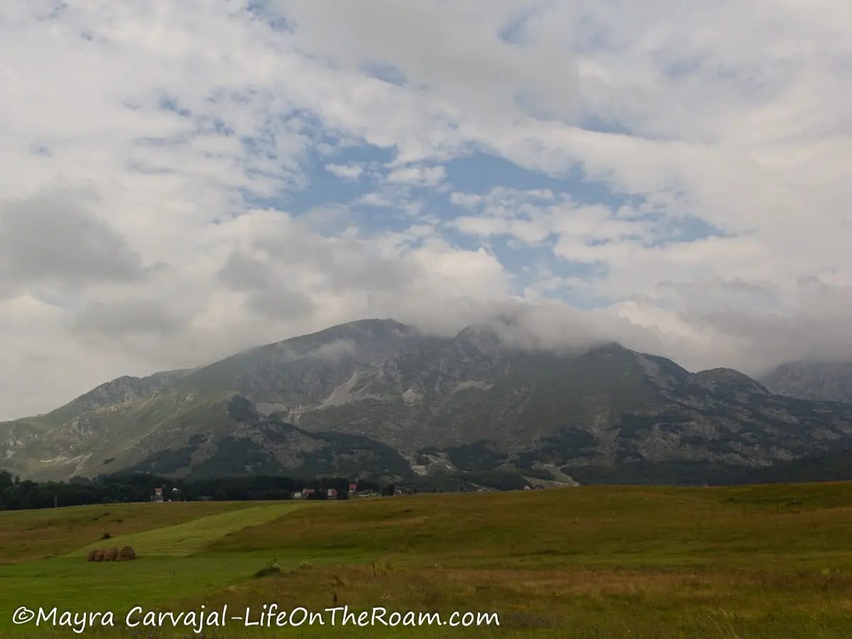 A traingular mountain with the peak partially covered by a cloud and a meadow in the foreground