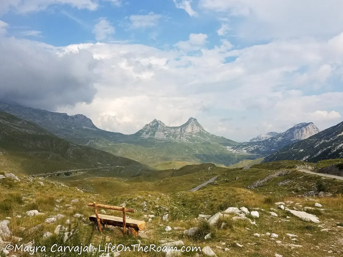 A bench in a grassy valley looking at a twin peak mountain in the distance