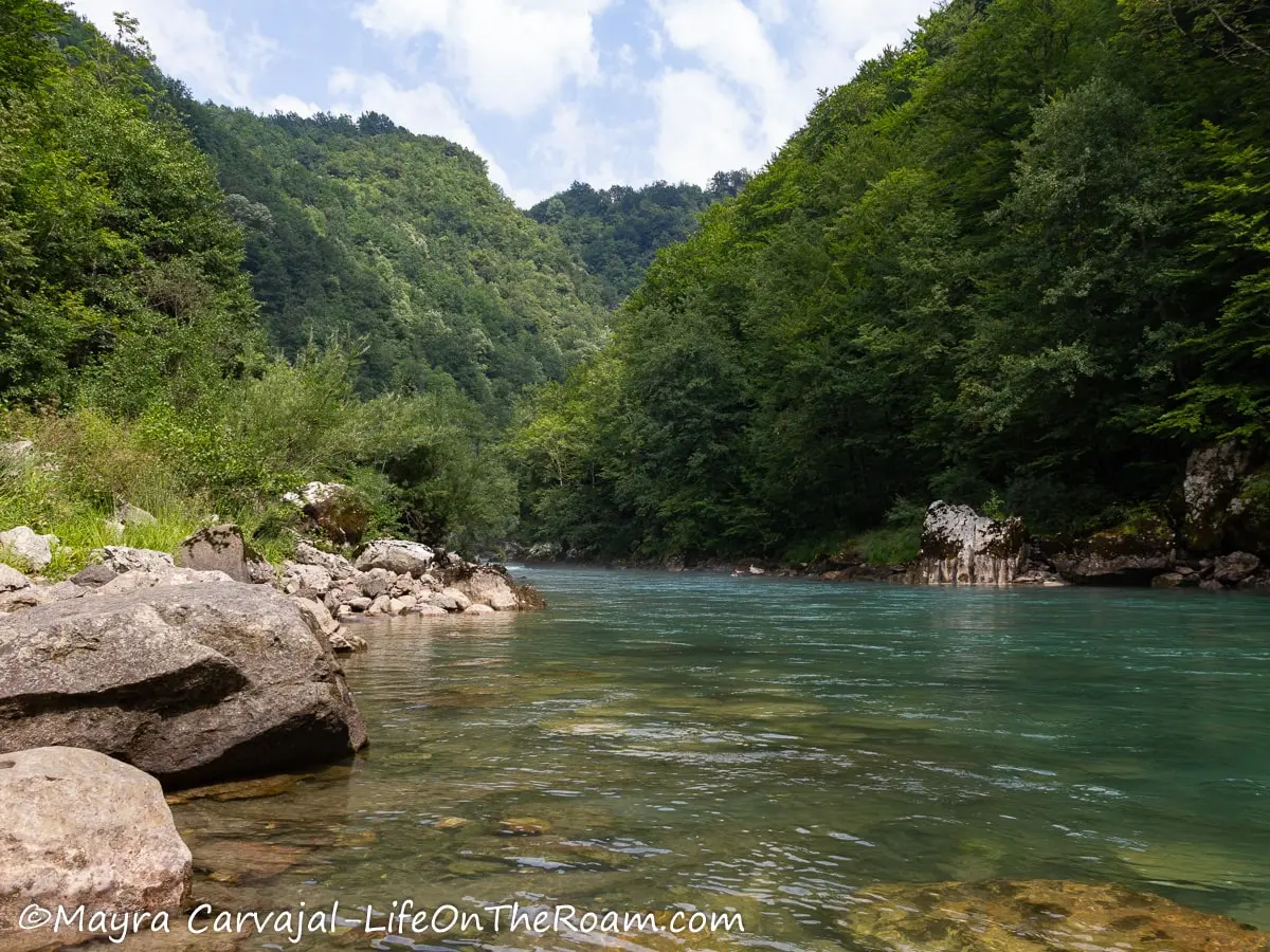 View of a turquoise river from the riverbank, surrounded be green mountains