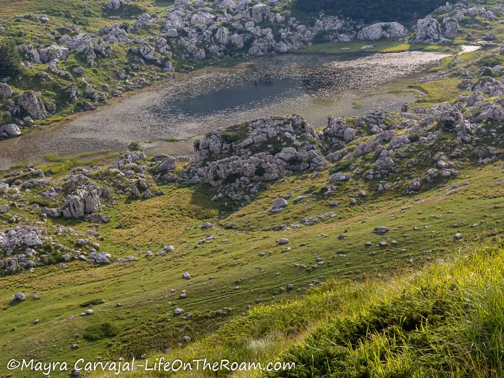 A small lake in an oval shape surrounded by big rocks and grassy hills