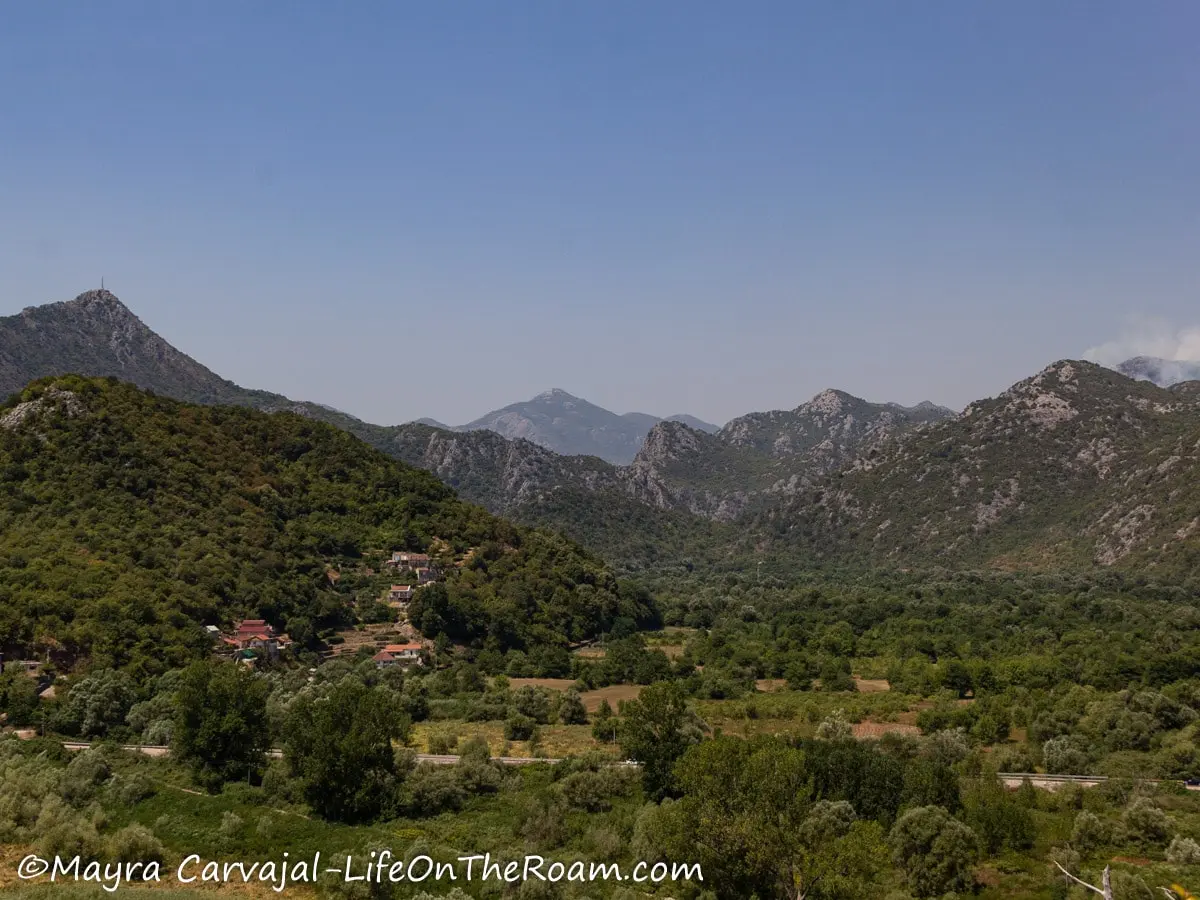 View of a valley with a few houses and tall mountains in the background