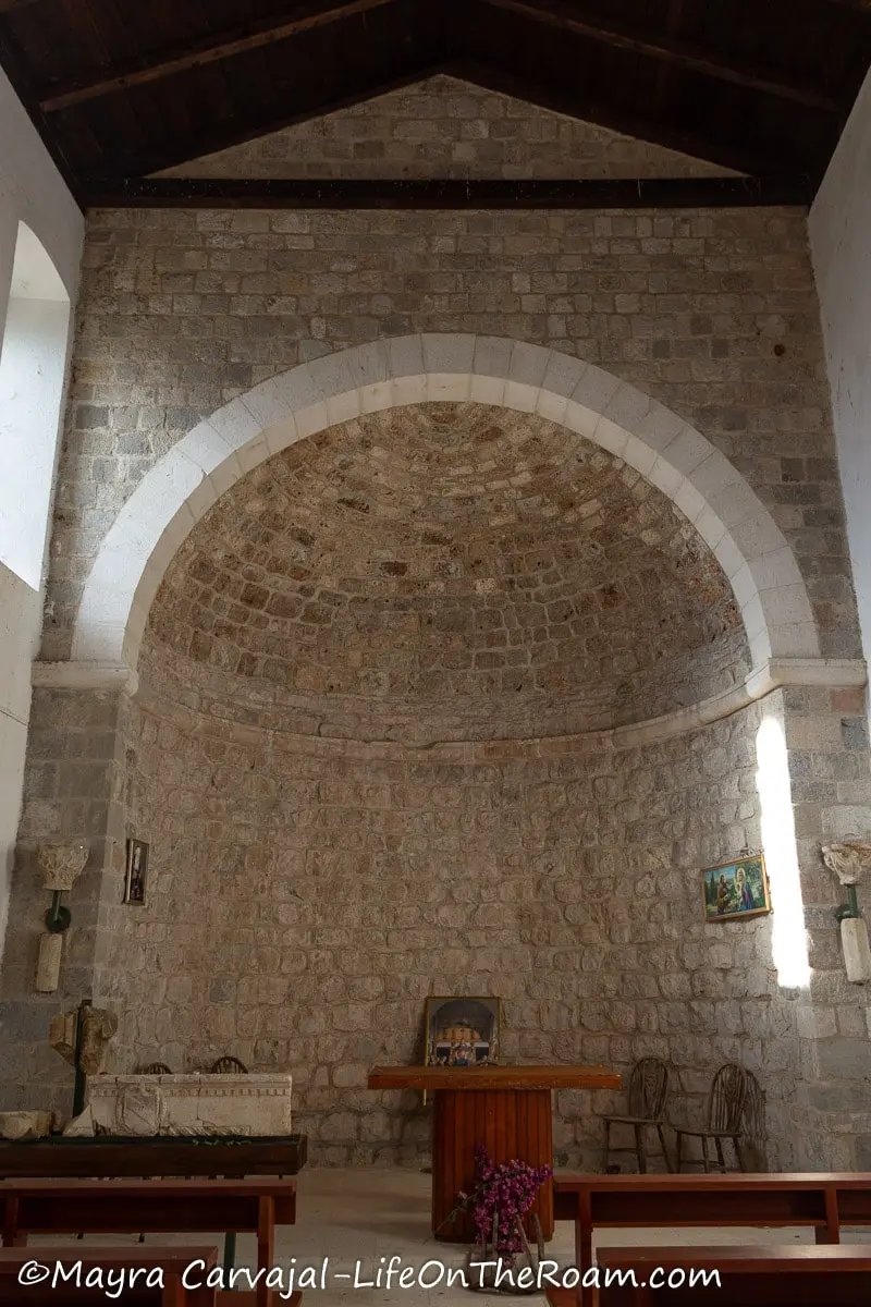 The apse of a stone church with a wood roof and a few pews