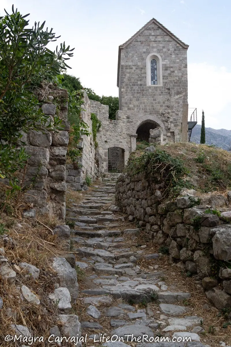 A stone stair leading to an ancient stone church with an entrance arch and a narrow long window above