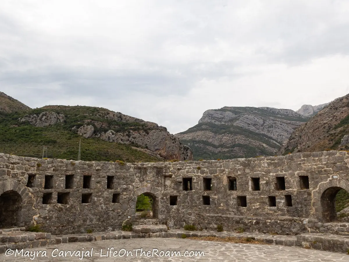 A wall with openings to fire canons and to shoot arrows, with a mountain in the background