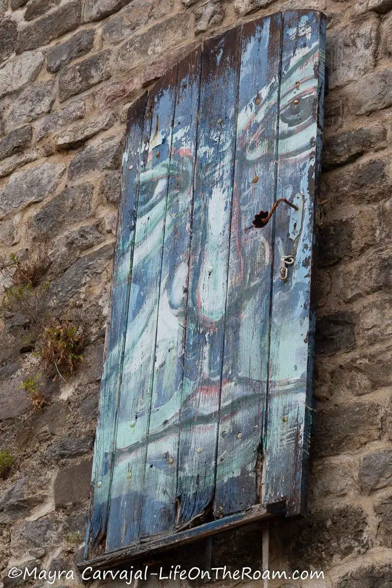 A wood door on a cut stone wall with the painting of a face on it