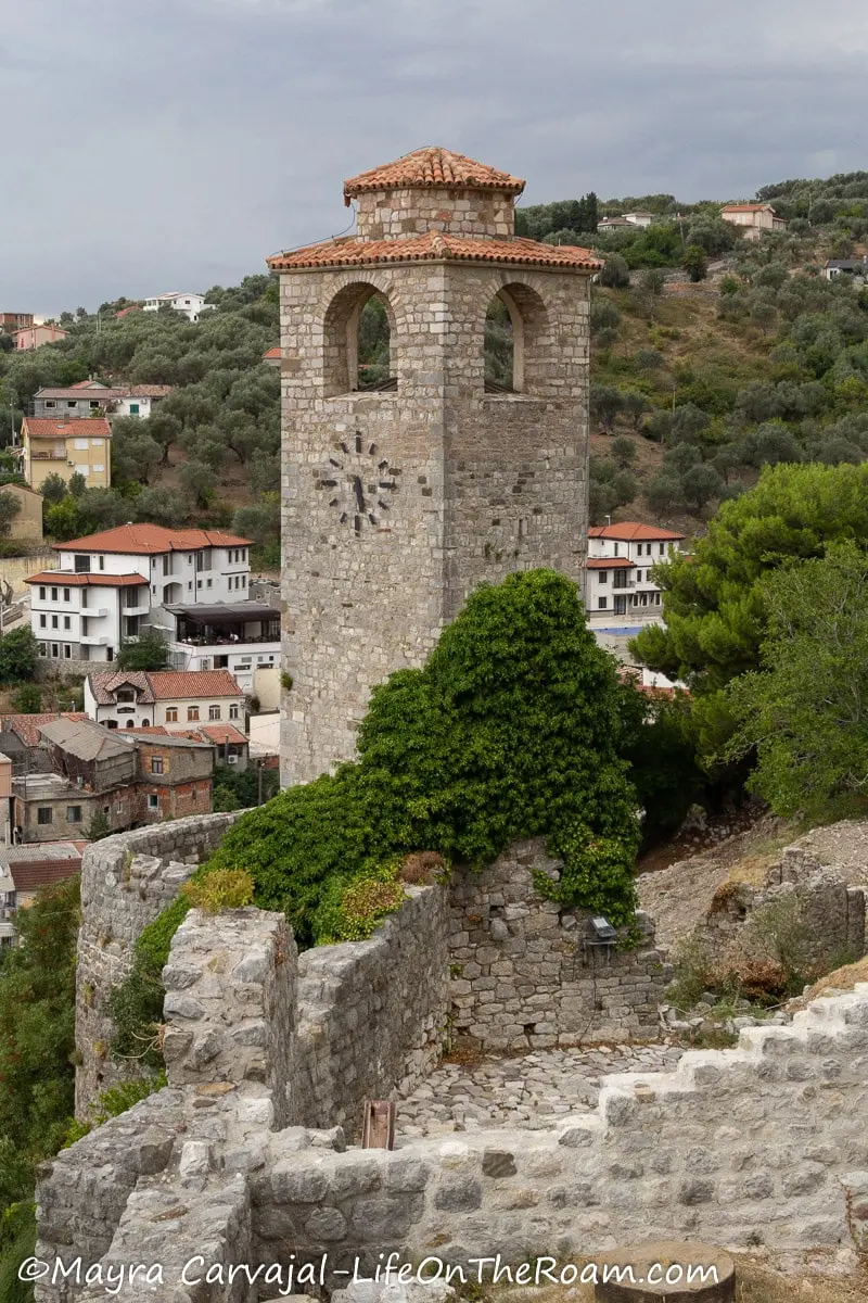 An ancient rectangular clock tower built with cut stone overlooking a town in the mountains