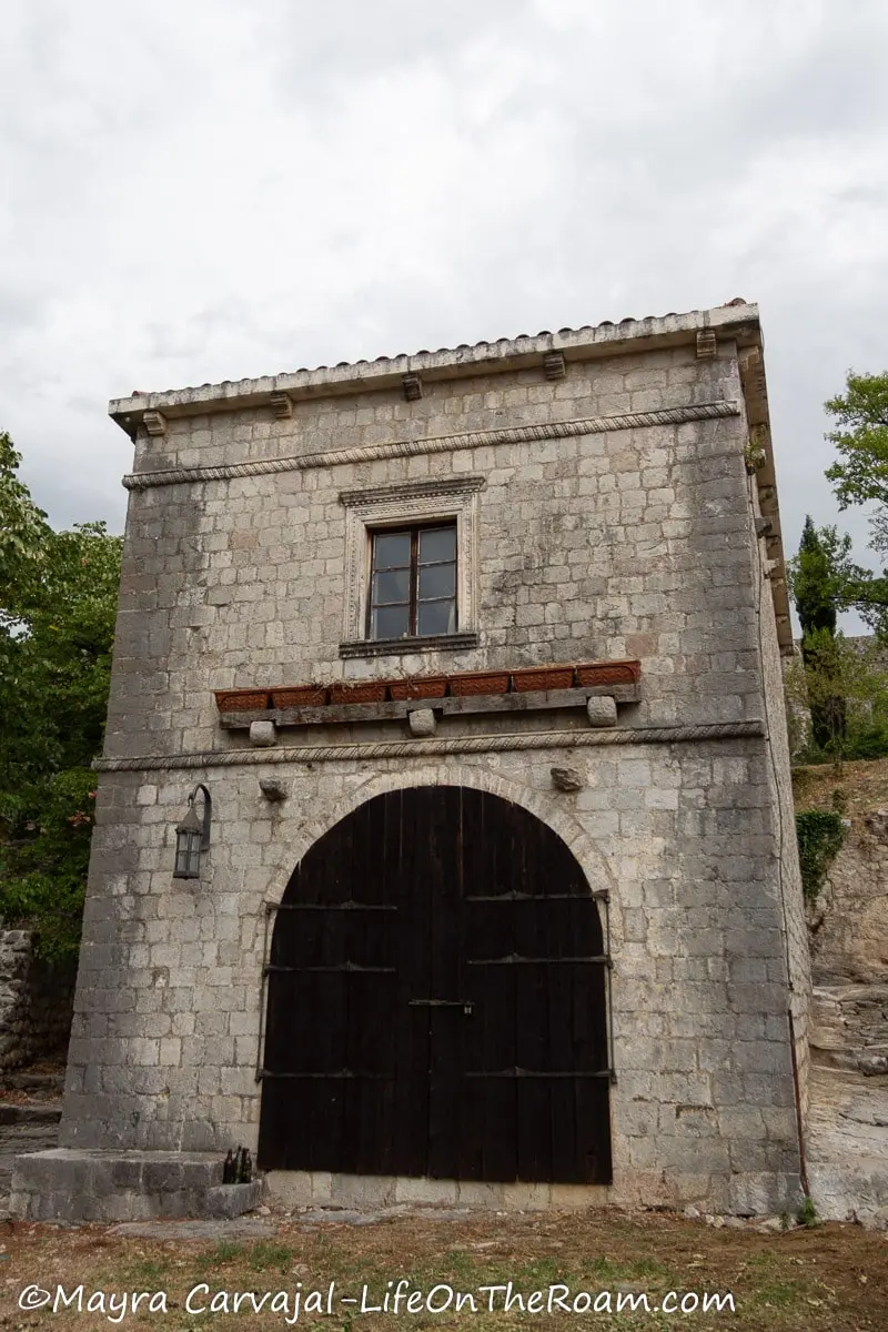 An old 2-storey rectangular building in stone with an arched double door and small window on the second floor