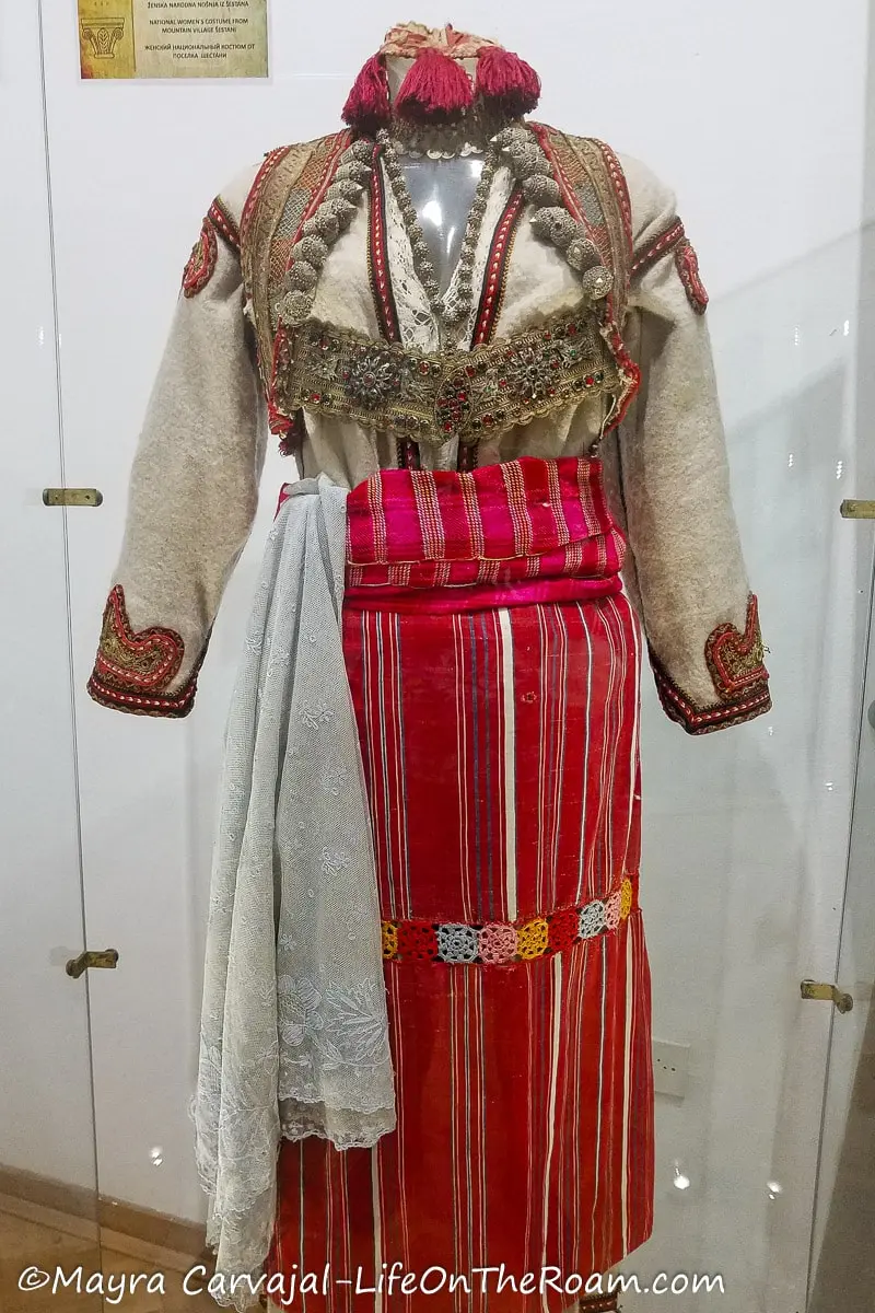 A women's traditional garment of Montenegro with long sleeves and elaborate metal embellishments, with a colourful longskirt in vivid purples