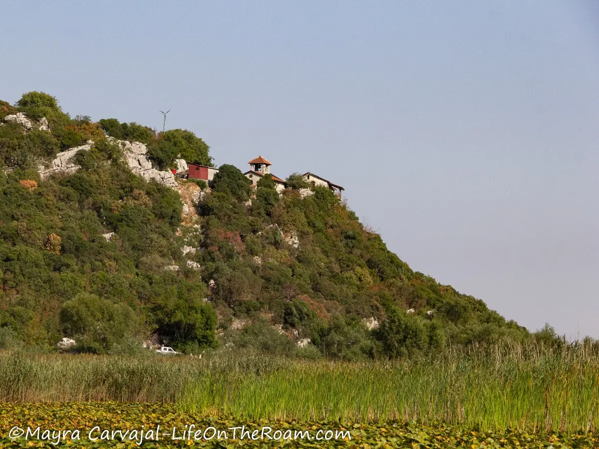 An ancient monastery at the top of a tall verdant hill and marshes in the foreground