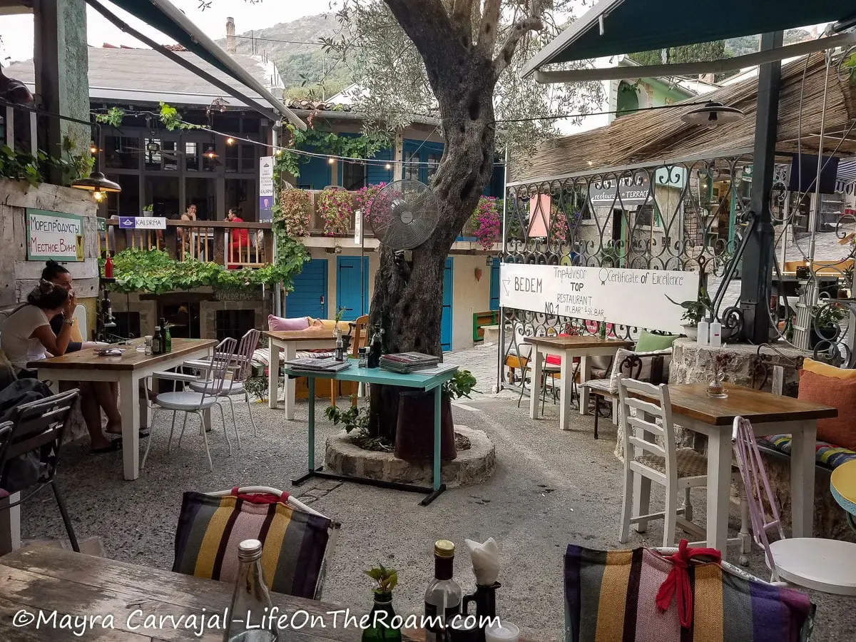 A terrace set around an olive tree with tables and chairs