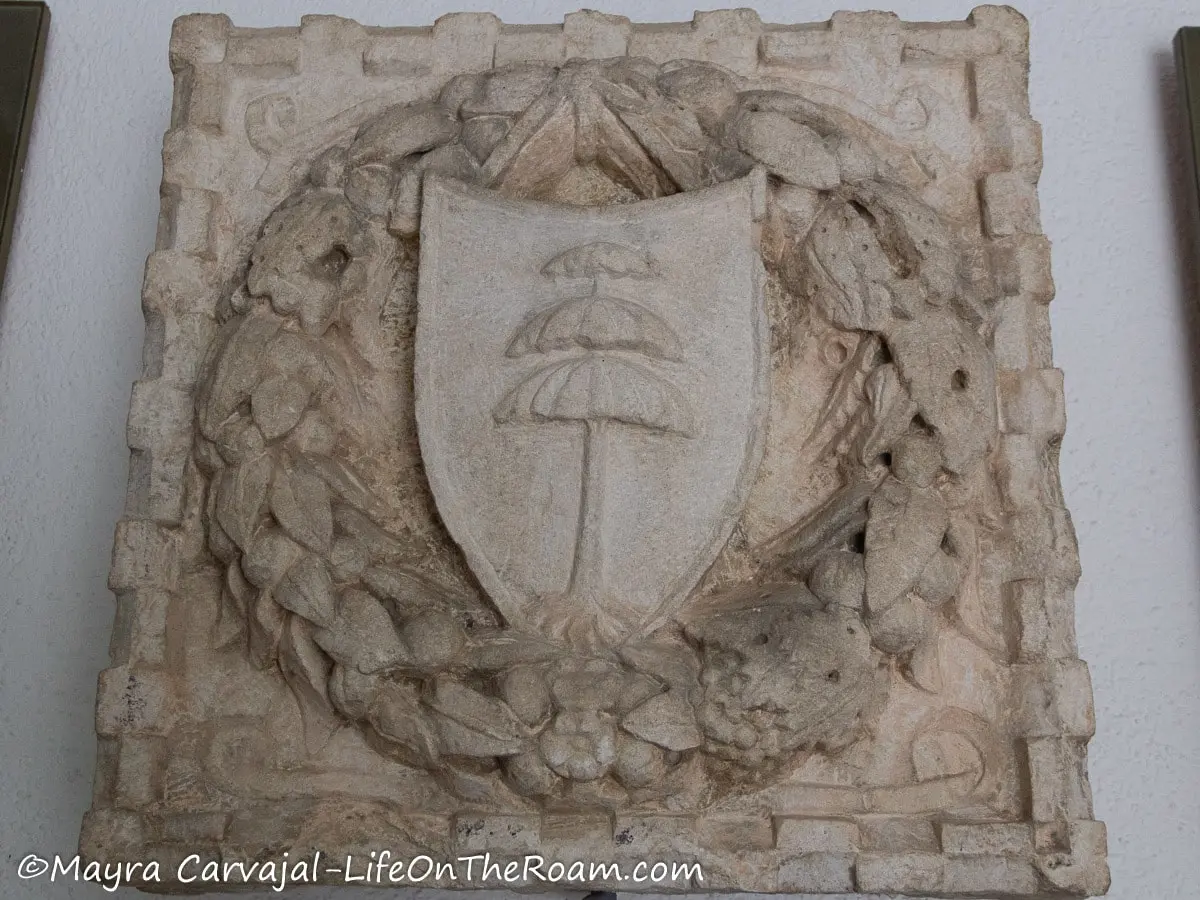 A wreath in stone with a shield inscribing a tree, all framed by a square in stone