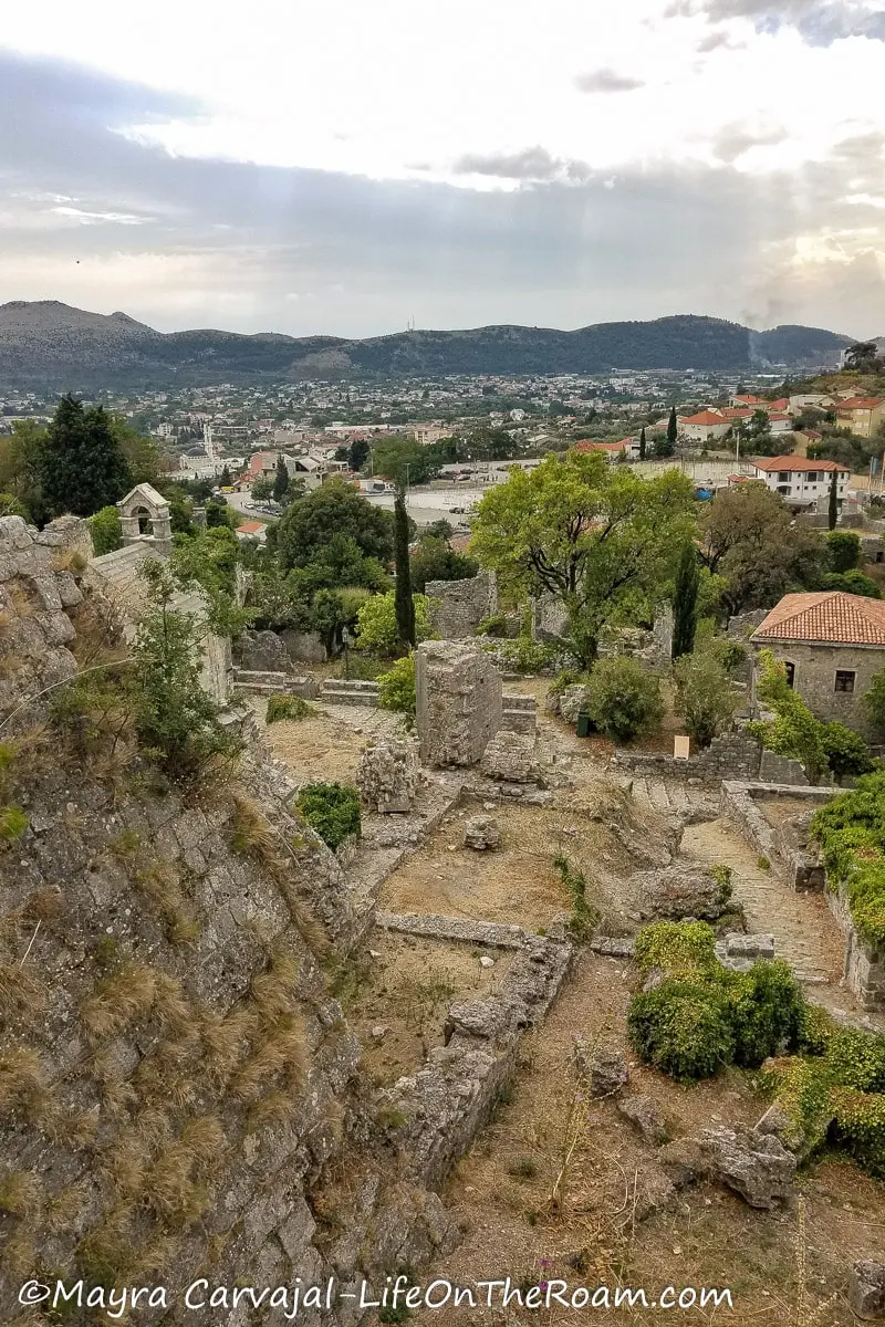 High view of the ruins of an ancient town with trees around and mountains in the distance