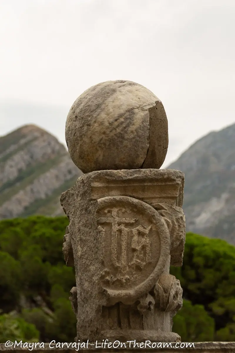 A relic in stone with old writing, with a stone ball on top and mountains in the background