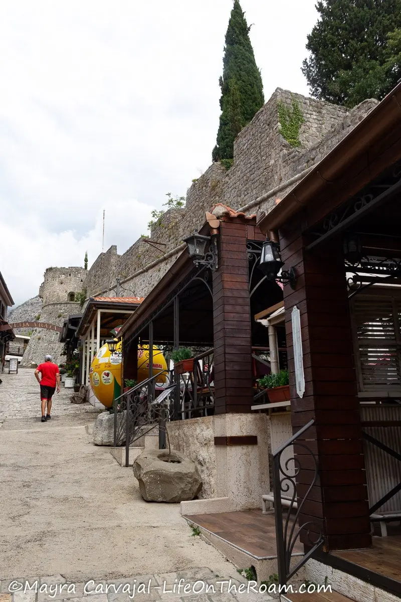 A man walking uphill on a cobblestone street lined up with terraces against an ancient tall stone wall