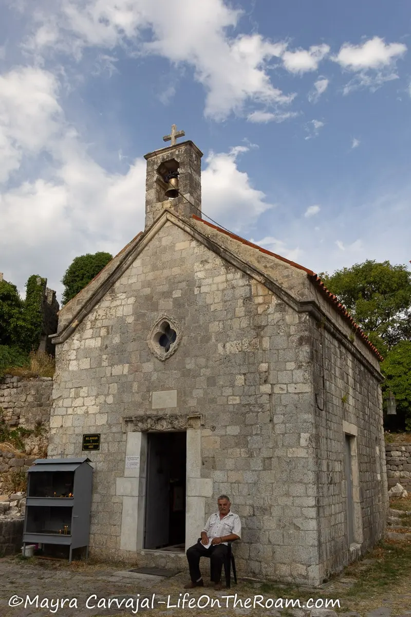 A small old stone church with a bell on top, a rosette and a small door