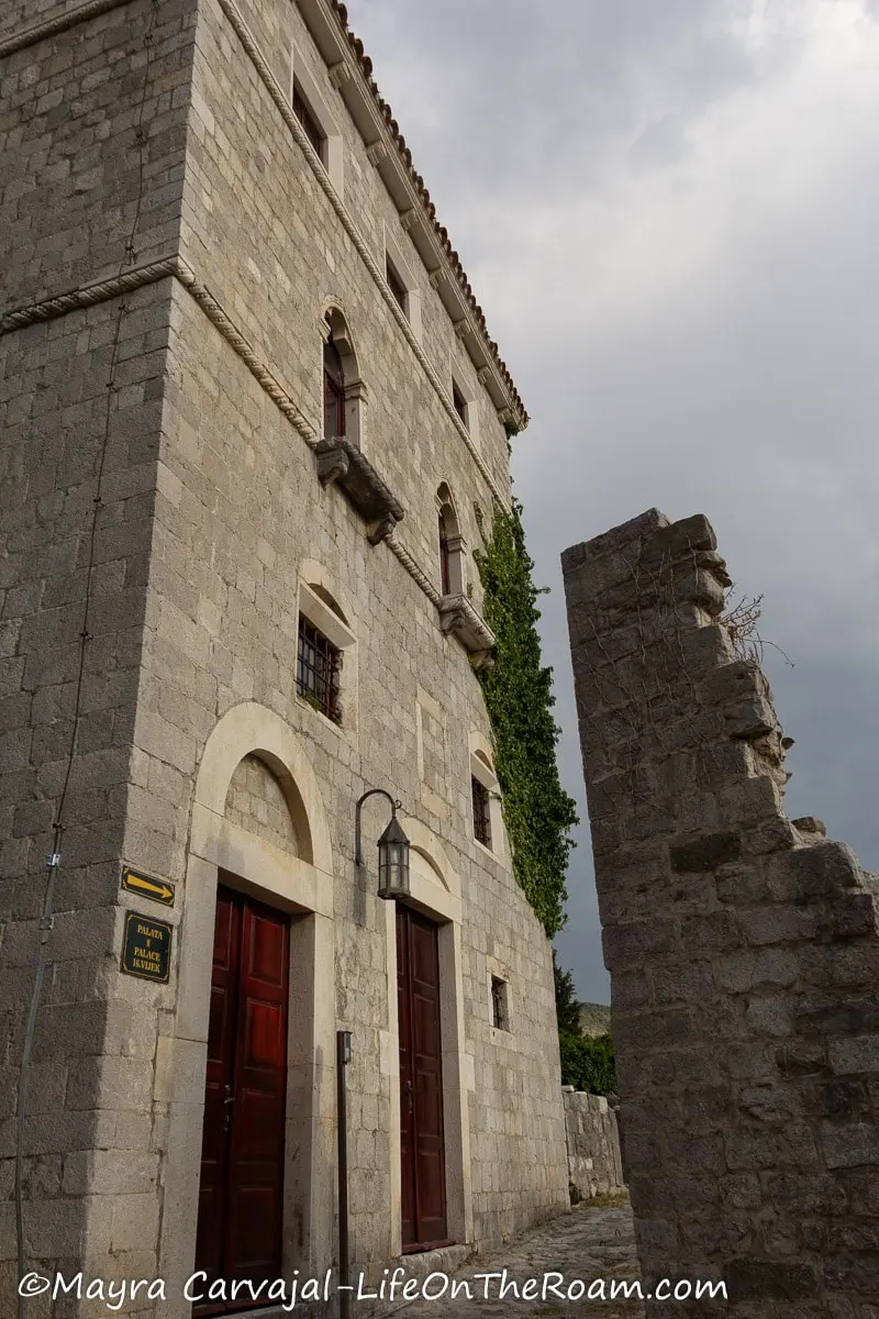 A 3-storey old building in stone with arched doors and small windows in the ruins of an ancient city