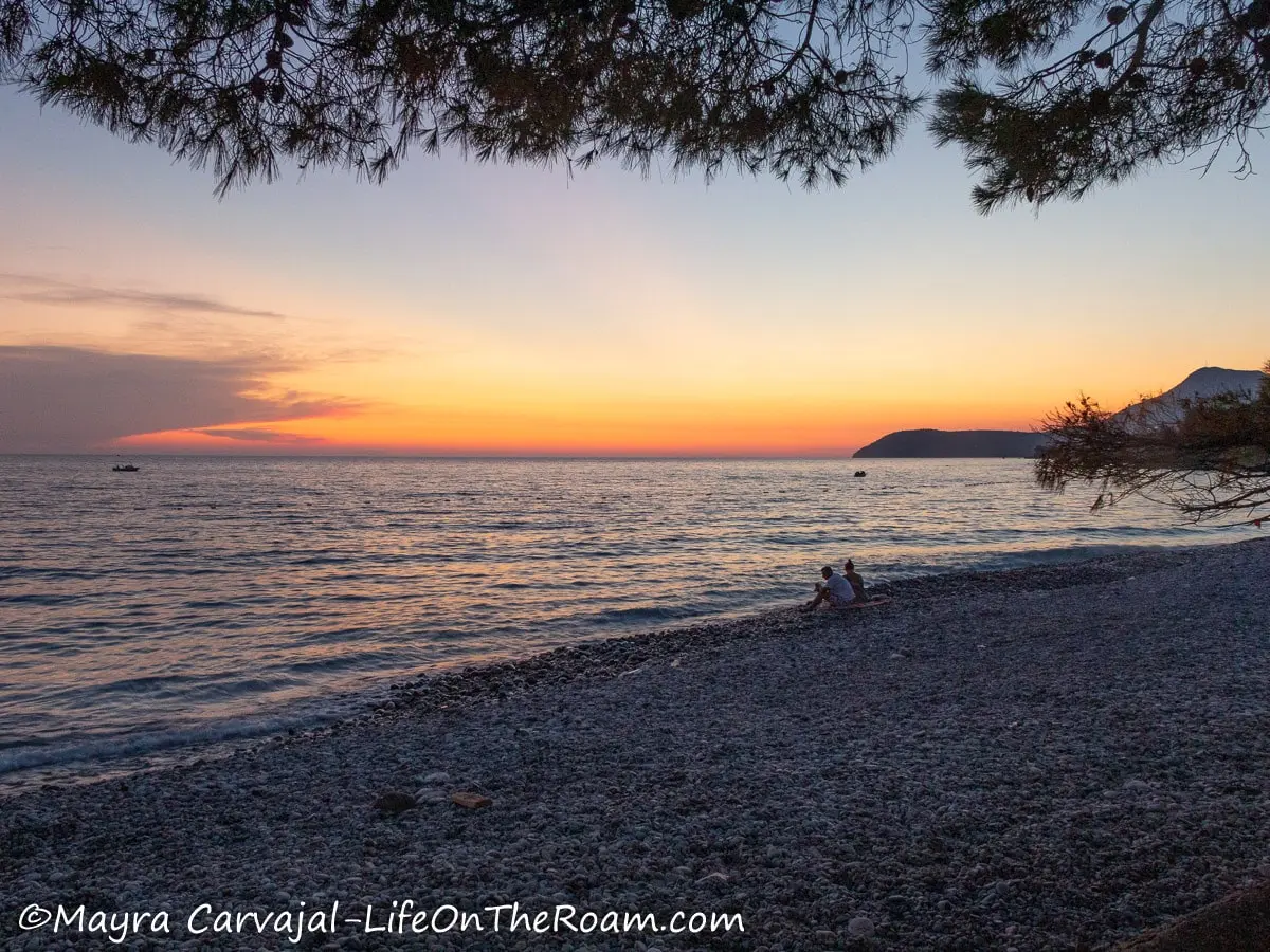 View of a sunset over the sea from a rocky beach with trees