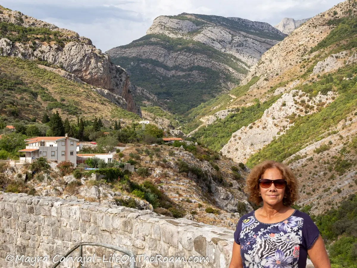 Mayra standing against a half cut stone wall with mountains in the background