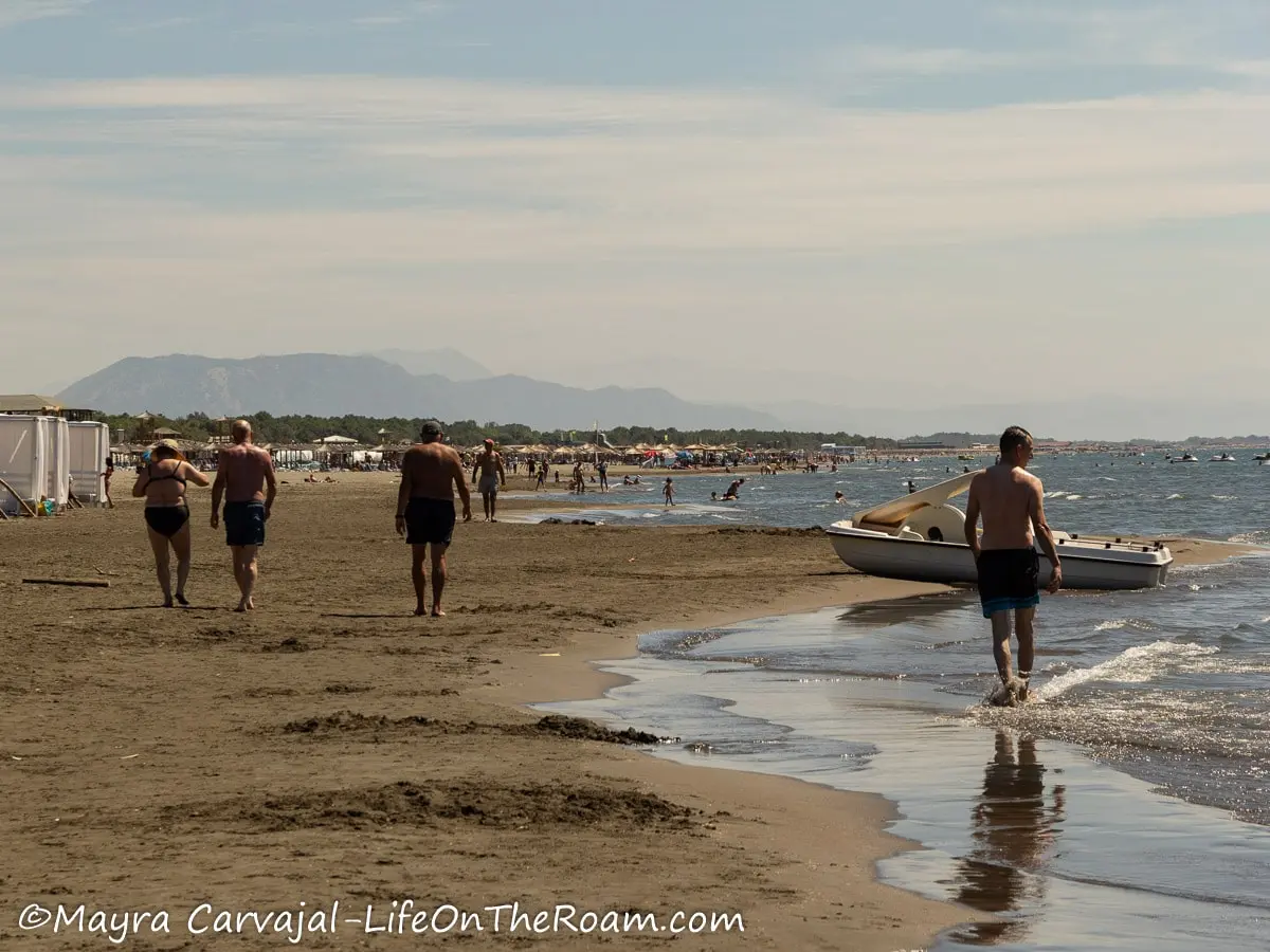 People walking on a sandy beach with dark sand with umbrellas along the way