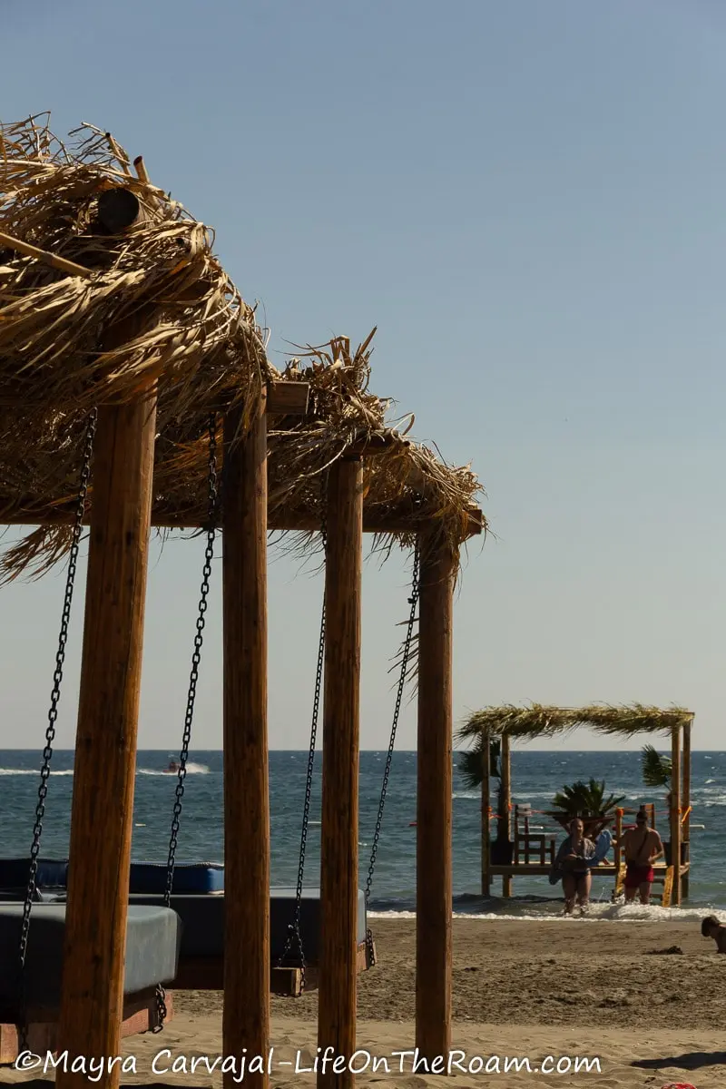 Beach beds suspended with metal cables on wood posts with palm roofs