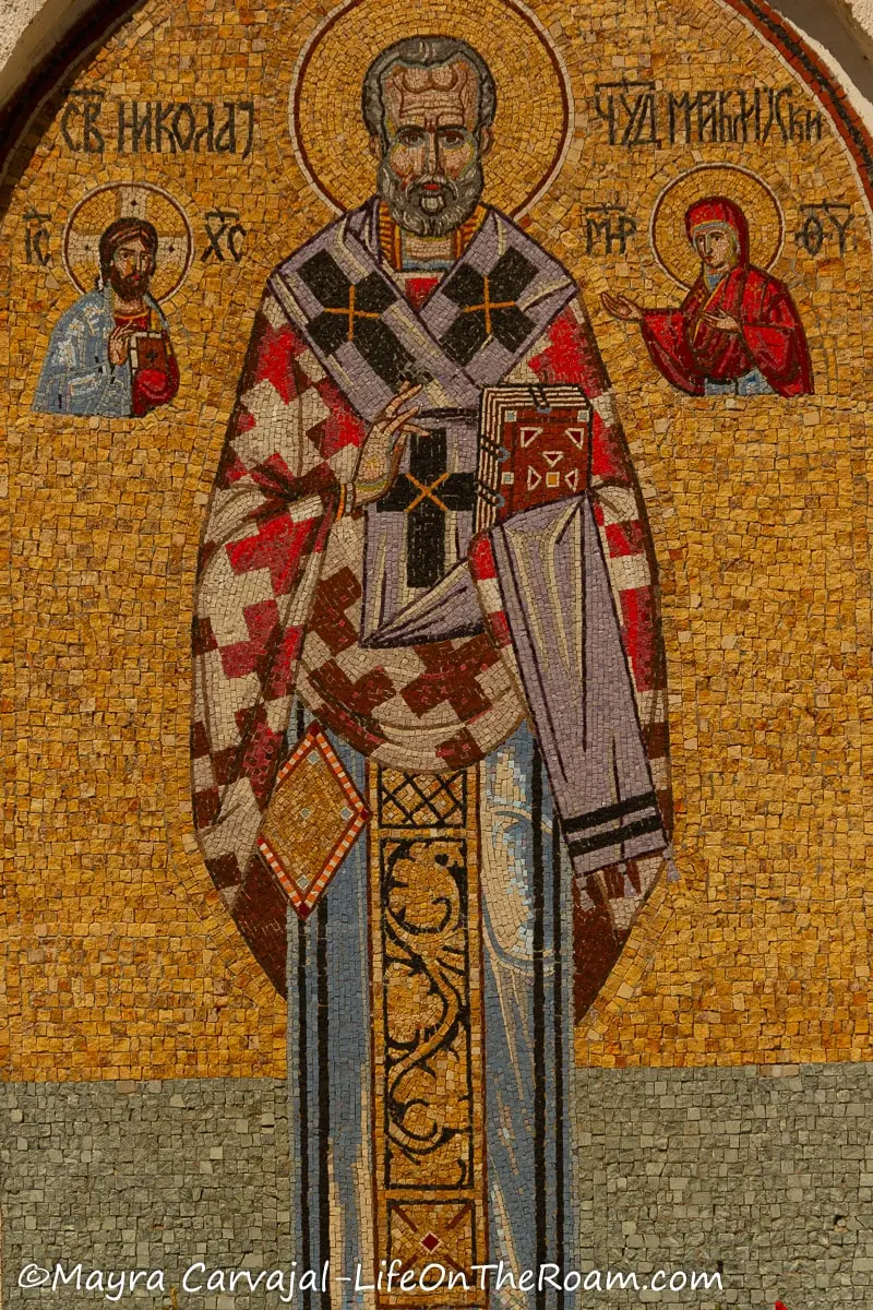 A mosaic depicting a saint of the church with a colourful robe against a golden background