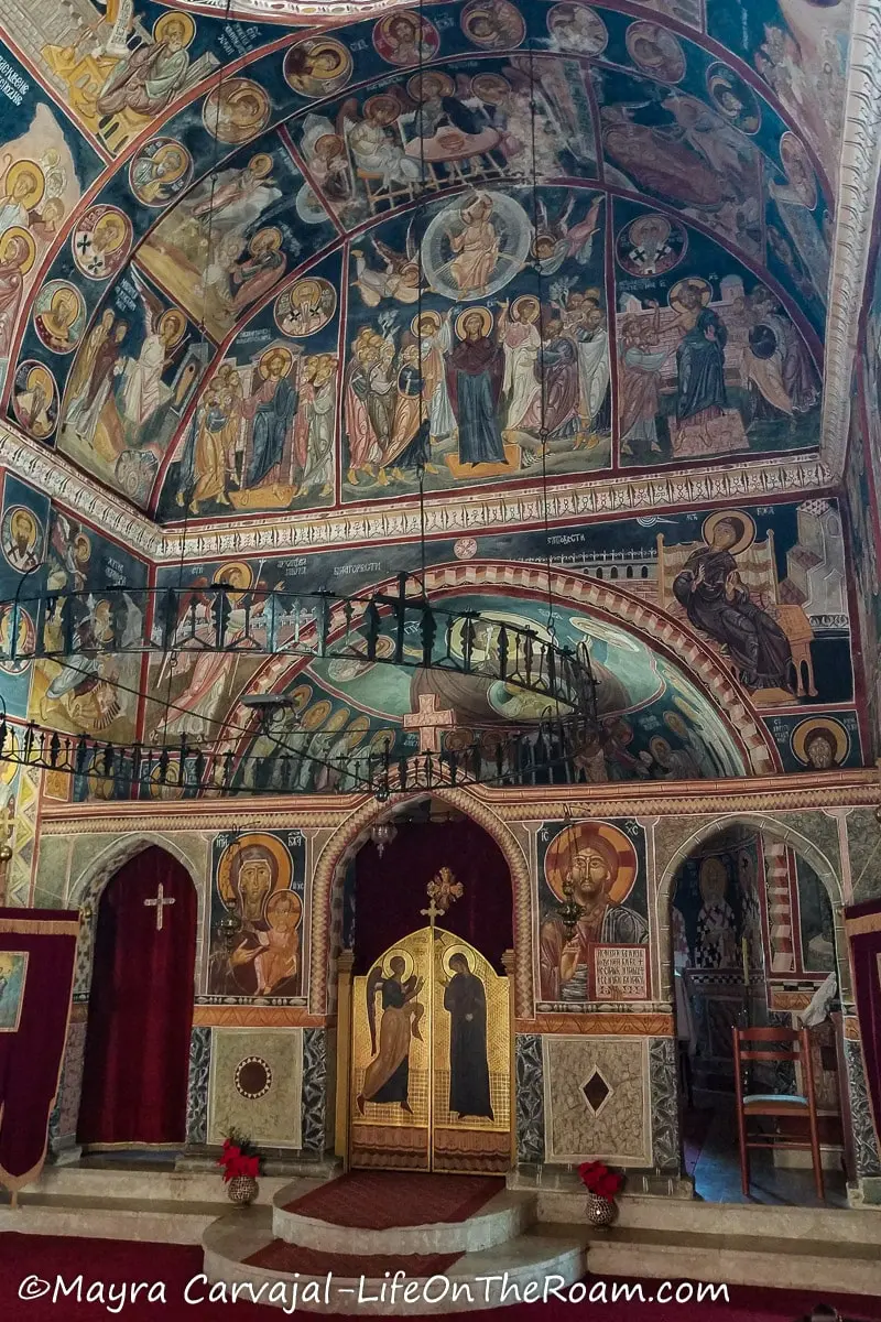 Frescoes depicting saints and biblical figures covering the walls and ceilings of an Orthodox church, with a deep blue background and a round metal chandelier in the front