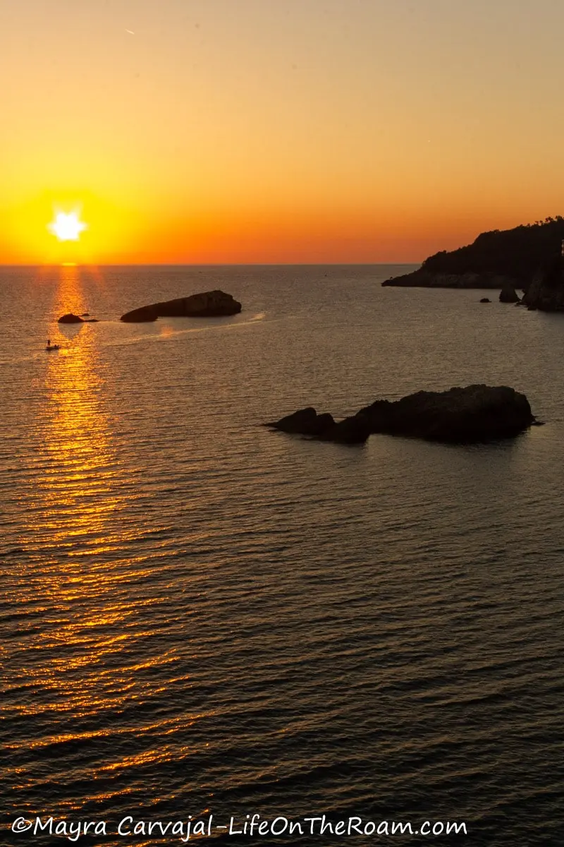 View of a sunset over the sea with big rock formations, from a high point