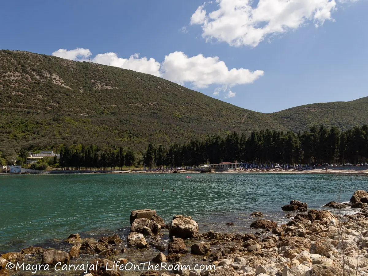 Distant view of a beach  in a bay with pines behind, surrounded by hills