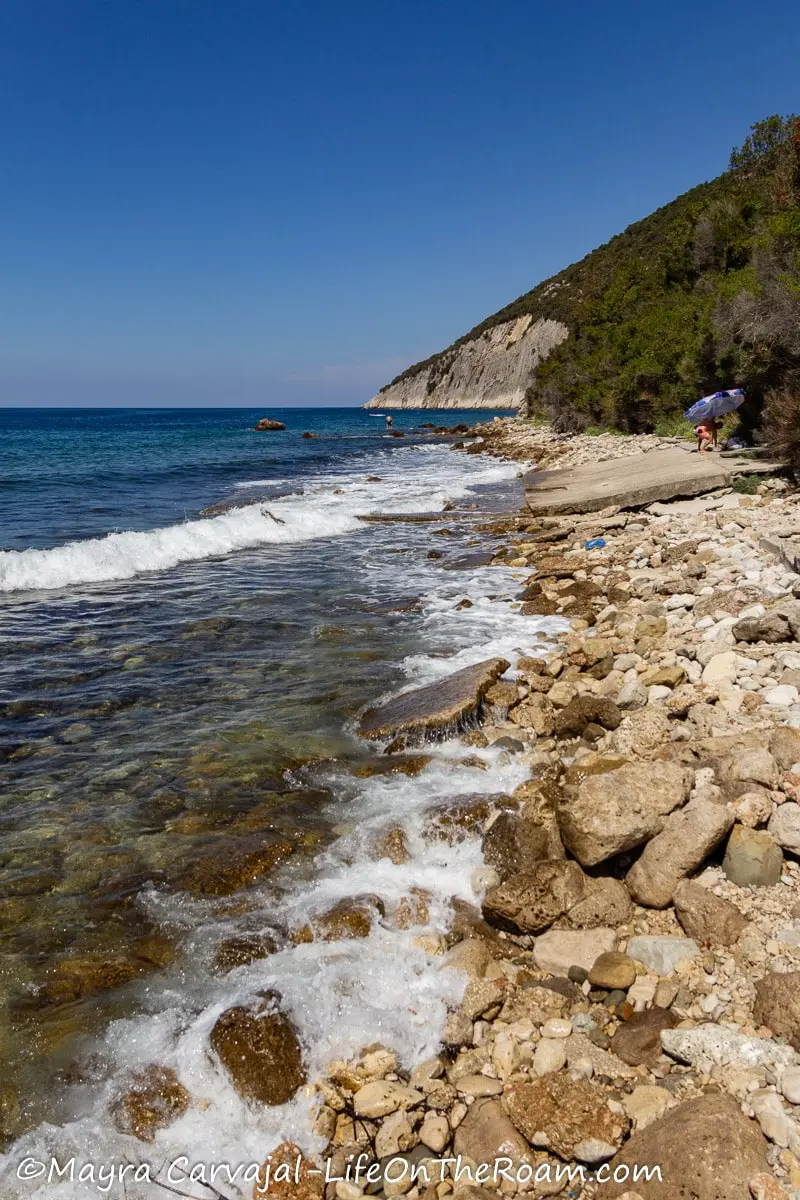 A coastline with big rocks and broken pieces of concrete on a beach at the foot of a hill