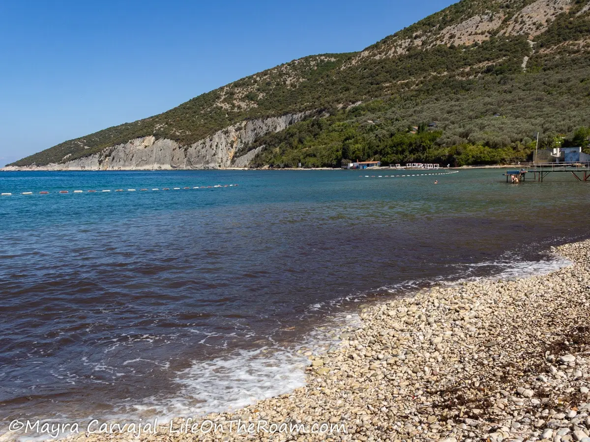 A rocky beach with different shades of blue with a mountain in the background