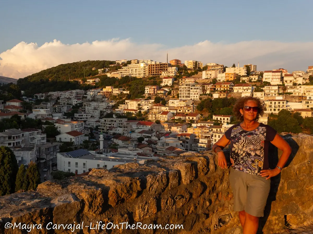 Mayra standing next to an old half wall with a view of a city built on a hill