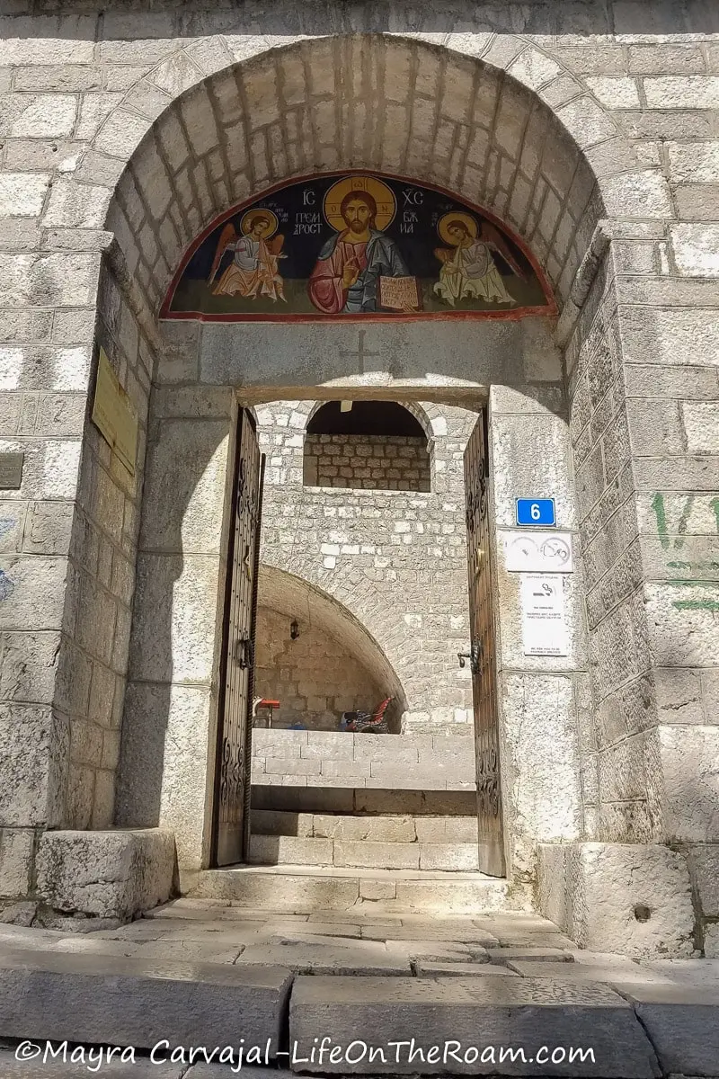 An arched entrance to an old monastery with a mosaic with religious figures at the top