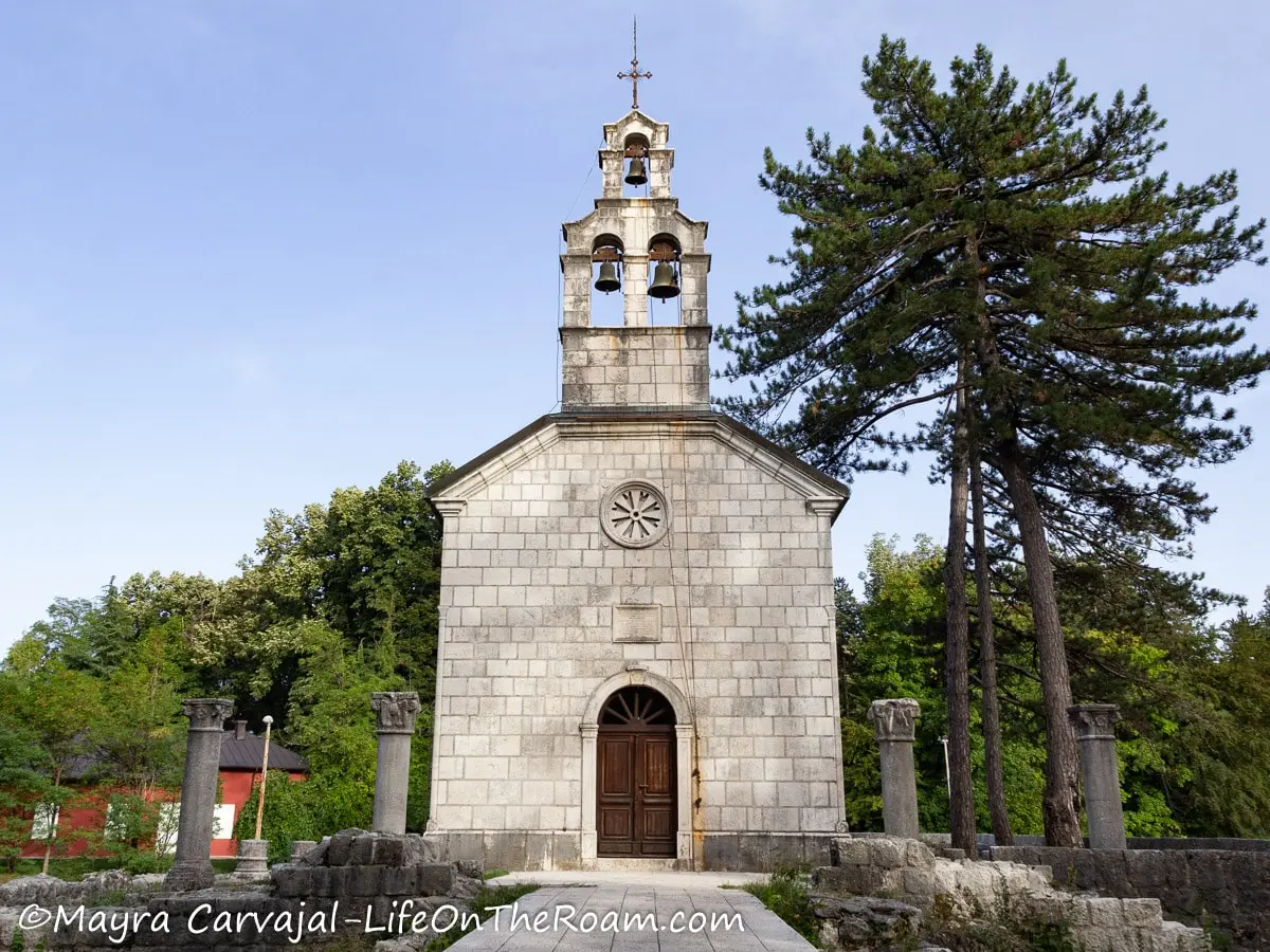 A small, old church with a tower with three bells and a cross on top, surrounded by classical columns