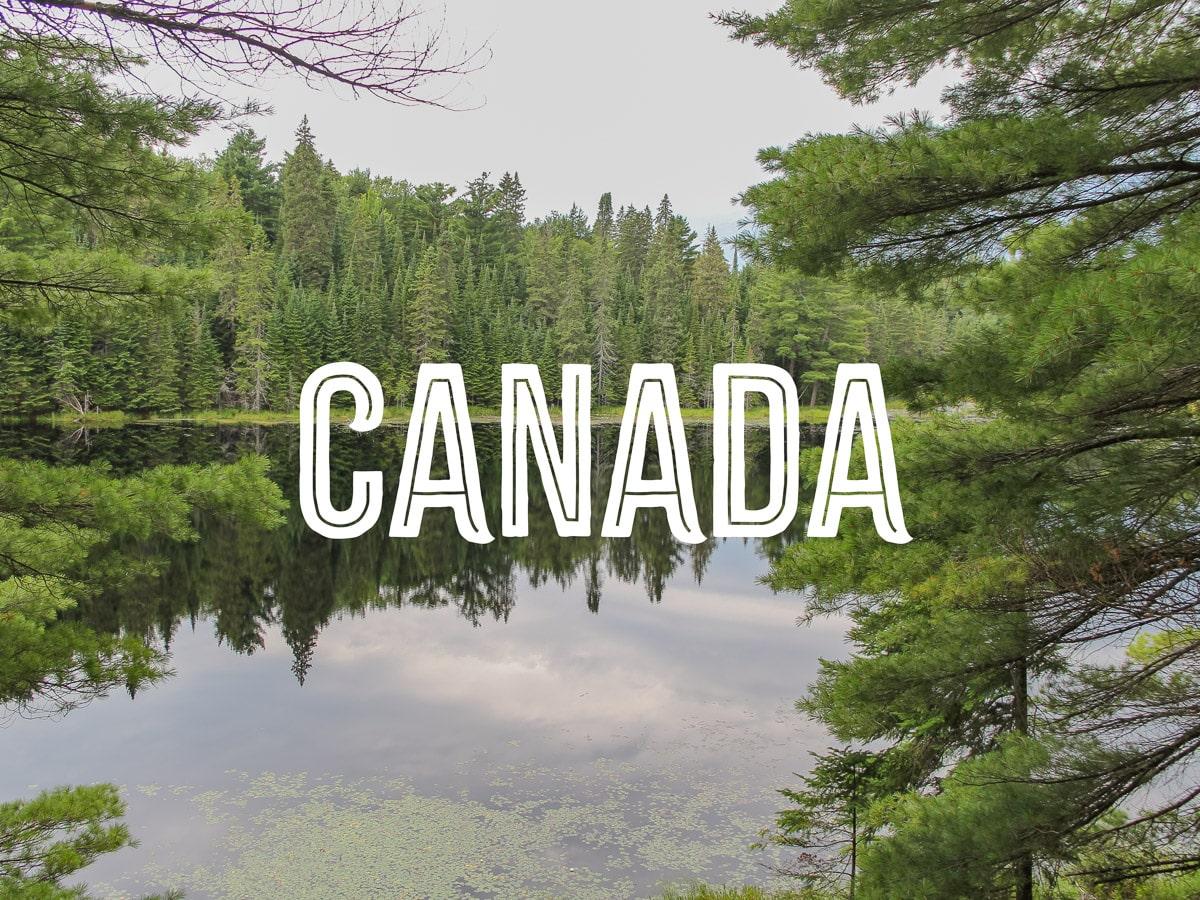 A pond where you can see the reflection of the surrounding pine forest with the word CANADA in the centre