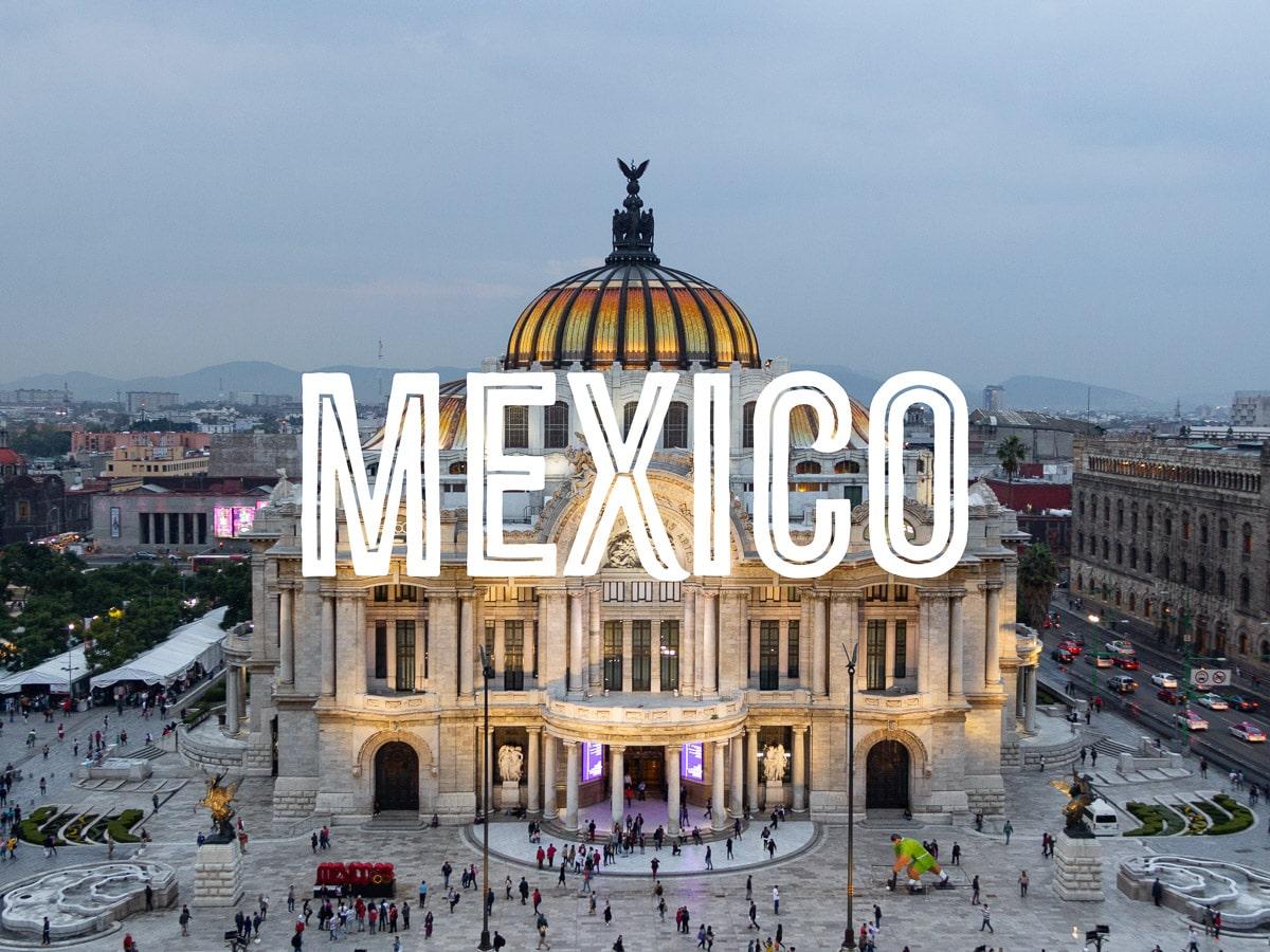 An Art Nouveau-style building with an illuminated dome in a busy square late afternoon, with the word MEXICO