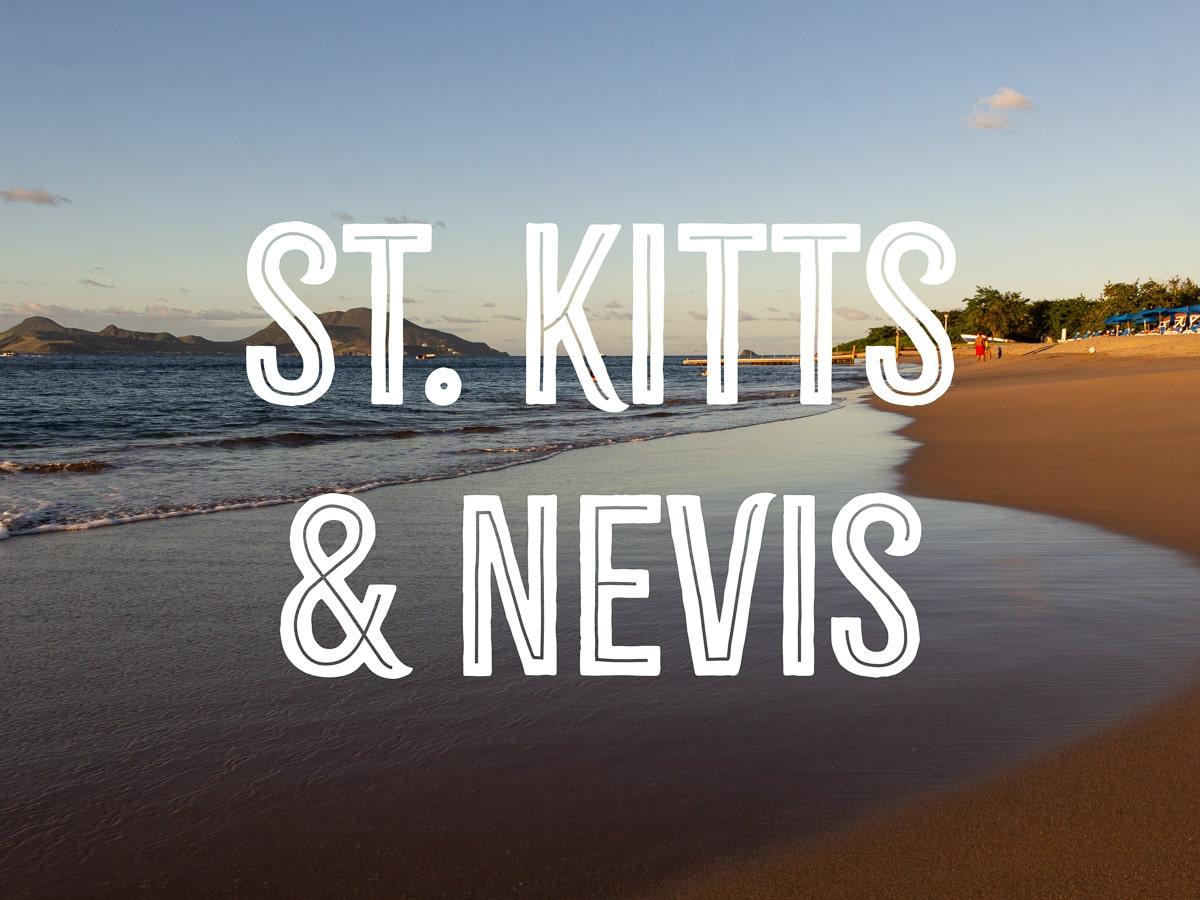 A beach with fine sand and a hill in the distance, with the words ST. KITTS& NEVIS