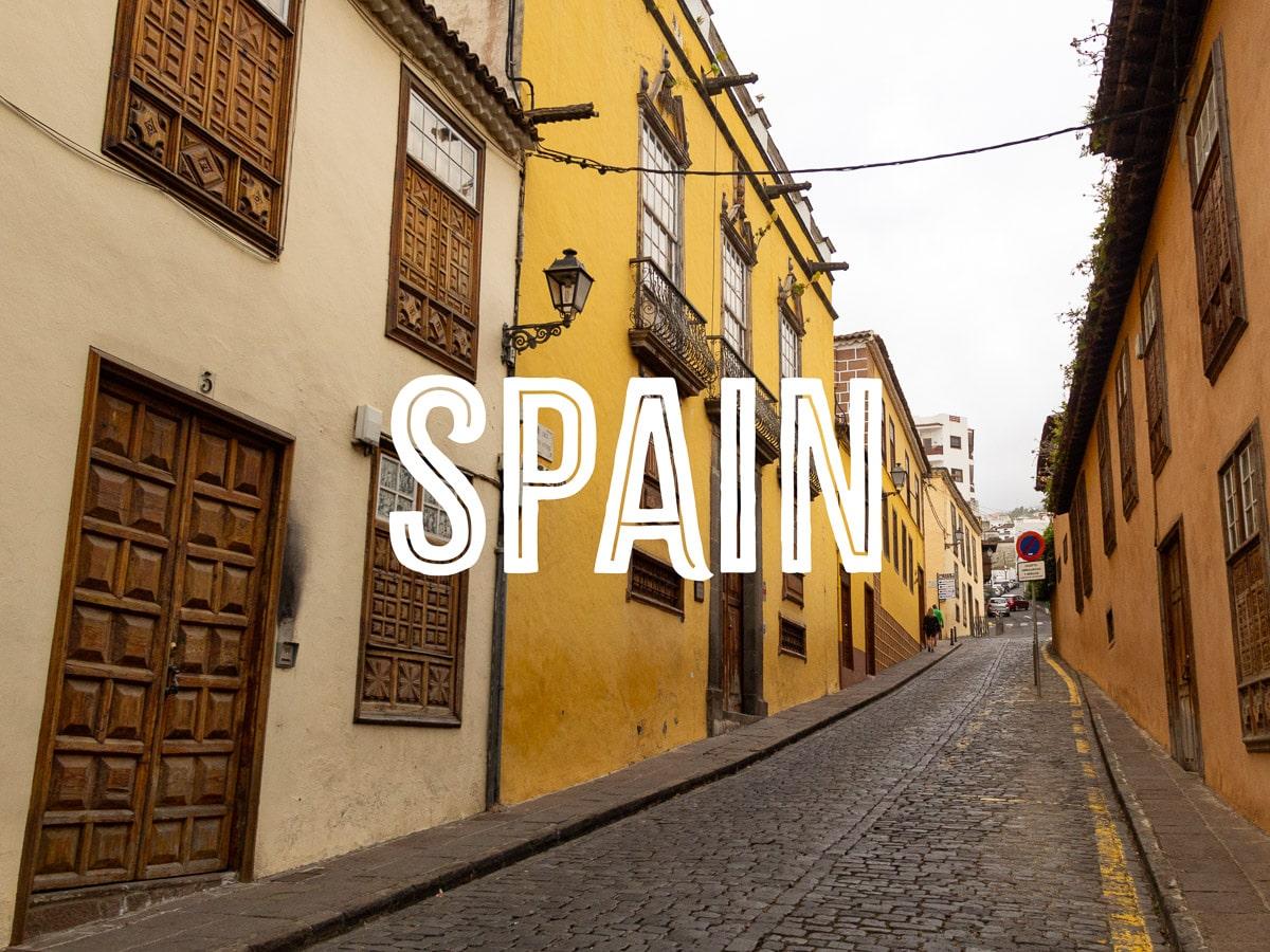 A cobblestone street with colonial-style two-storey houses on both side, with the word SPAIN