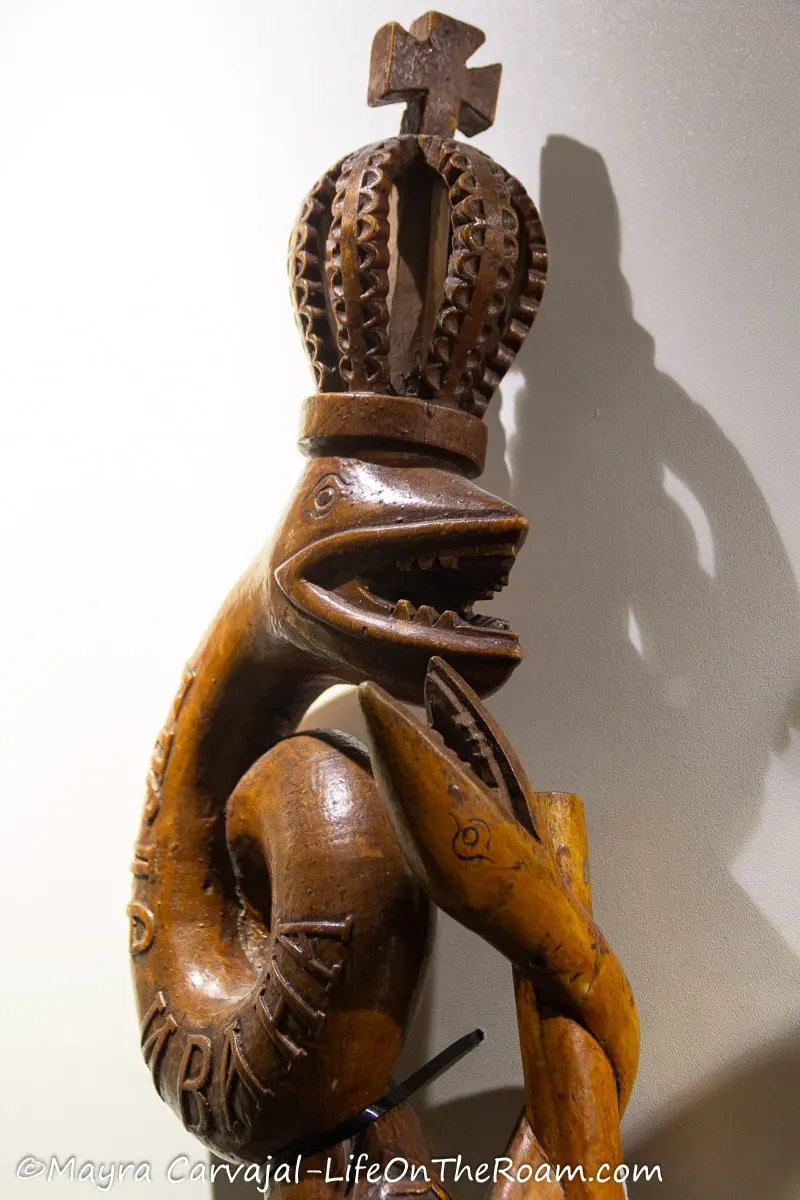 A wood handle of an instrument carved in the shape of a reptile and a serpent