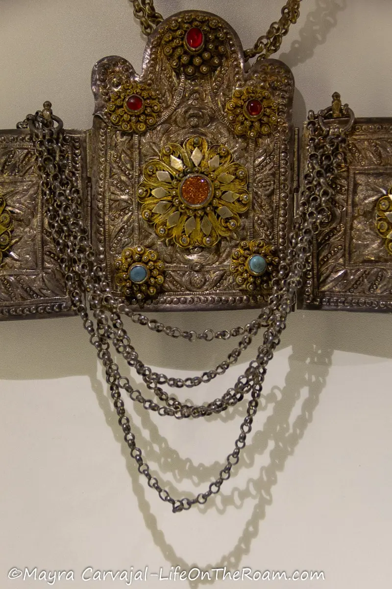 An intricate design on a belt made of silver with details in colour stones.