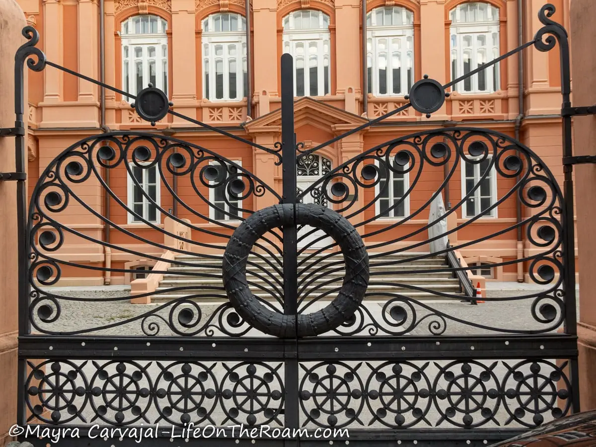 A black metal entrance gate with double leaf, adorned with swirls