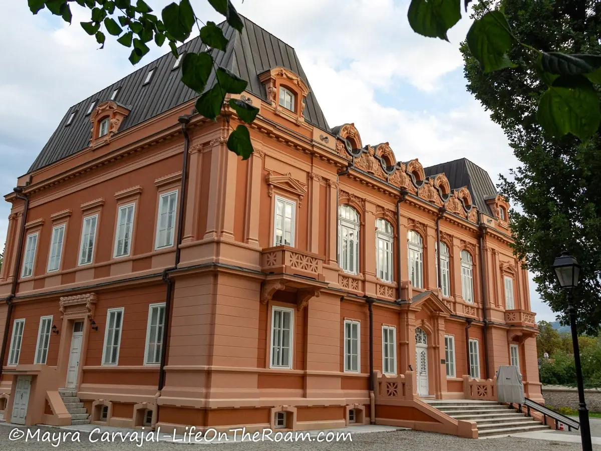 A large 2-story building in Baroque style with many windows and painted in dark pink tones