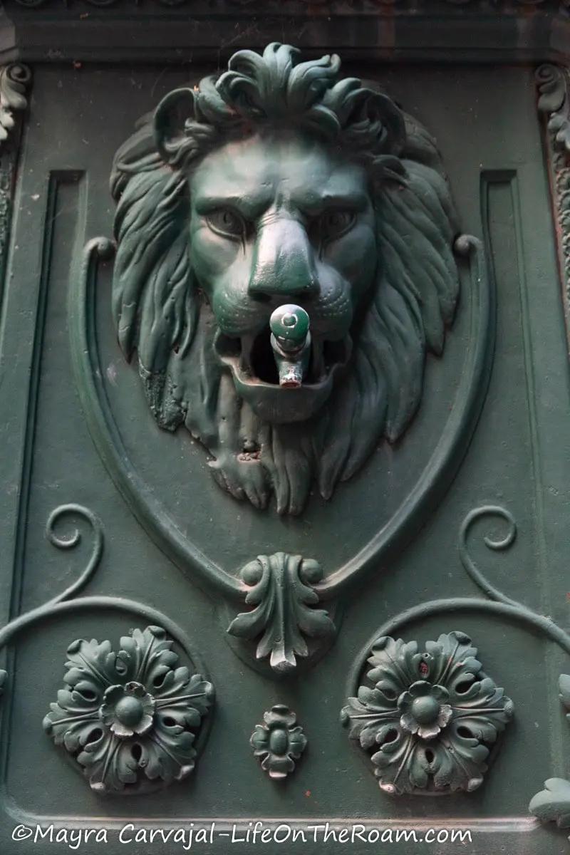 A fountain in metal with the head of lion framed by floral motifs