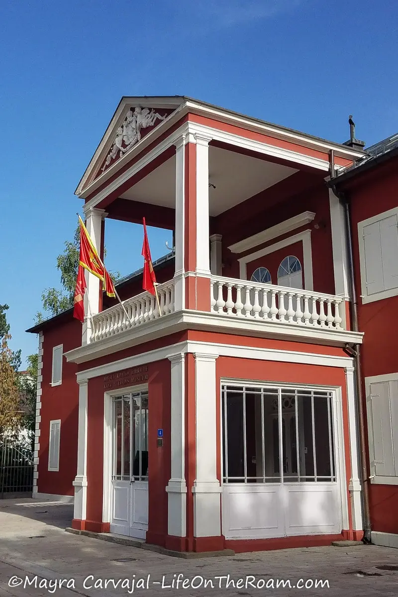 A 2-story house with a portico and flags, painted in bright pink and white