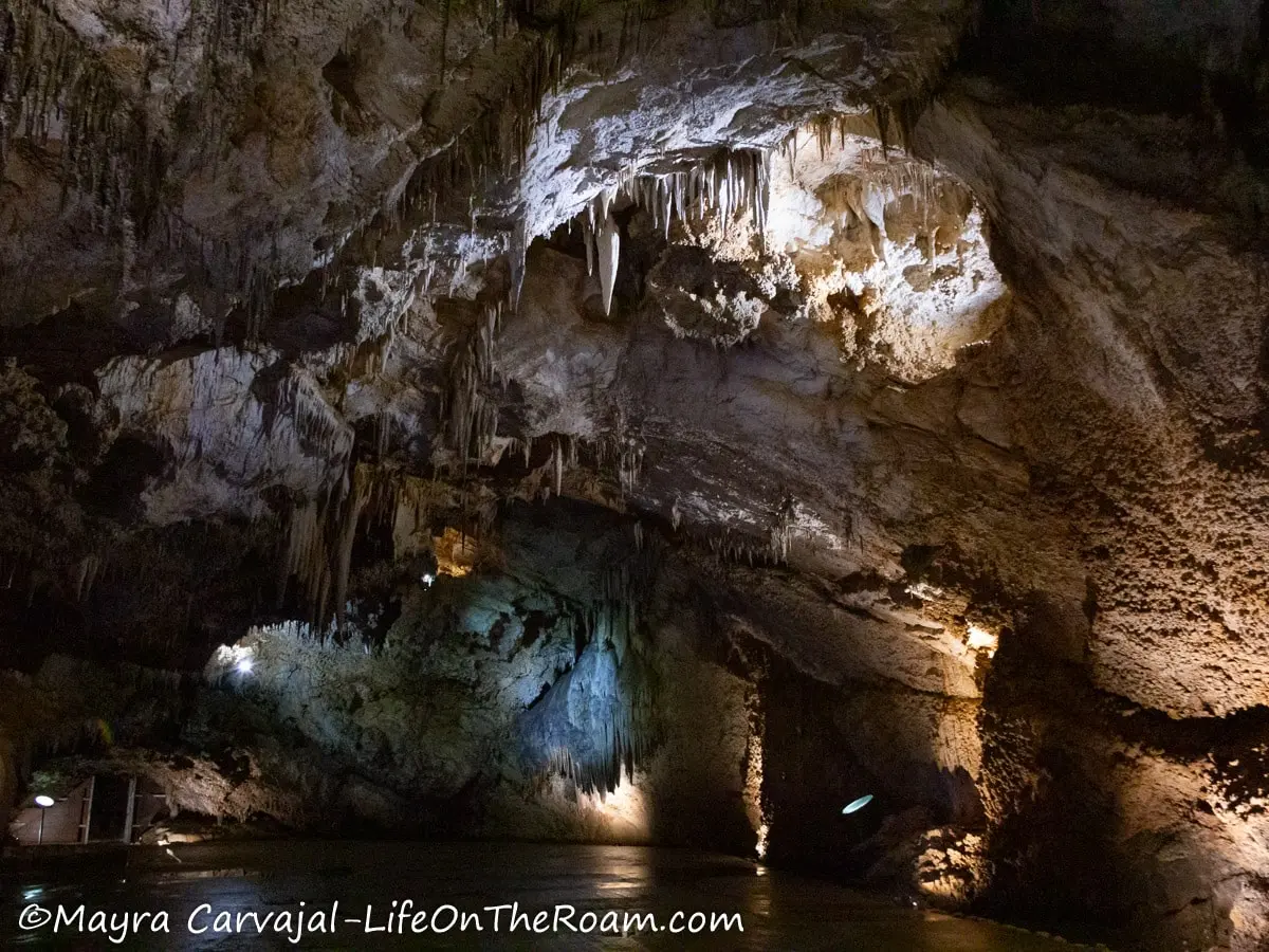 A tall and wide cave passage with spotlights and with different cave formations