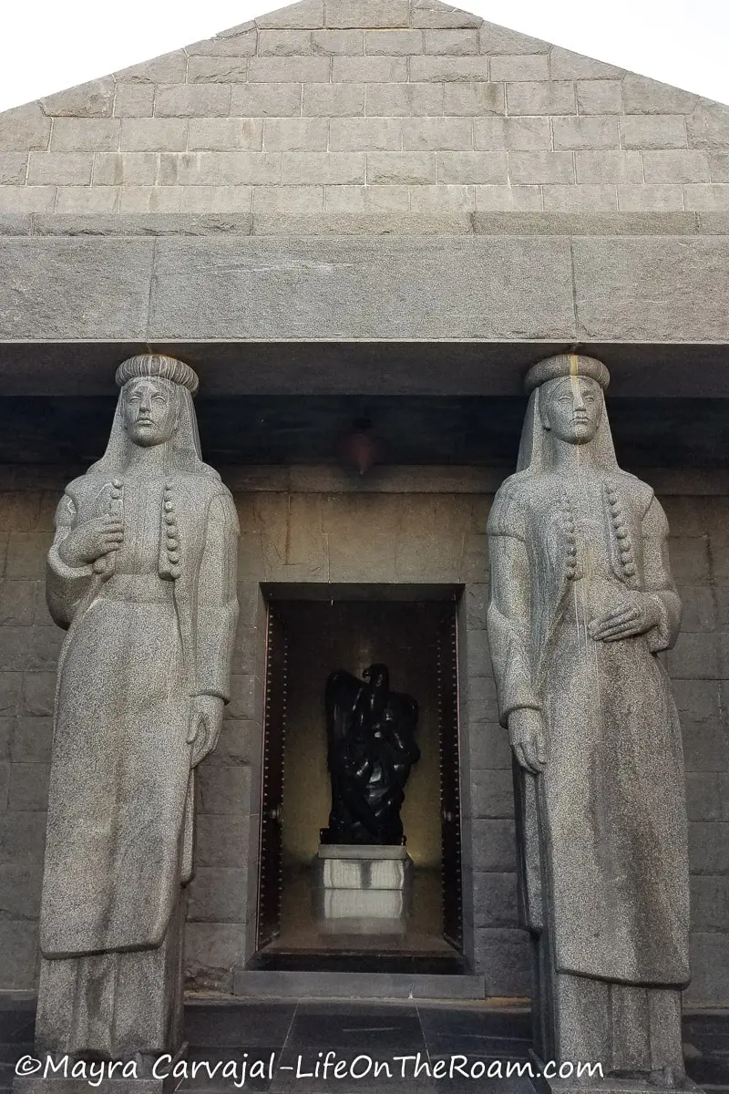 Two light gray granite statues depicting two guards standing at the entrance of a room in a mausoleum